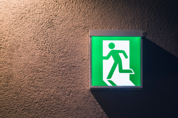 An illuminated emergency exit sign on a brown painted wall