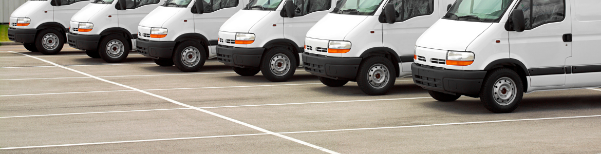 A fleet of white vans lined up in a warehouse depot car park