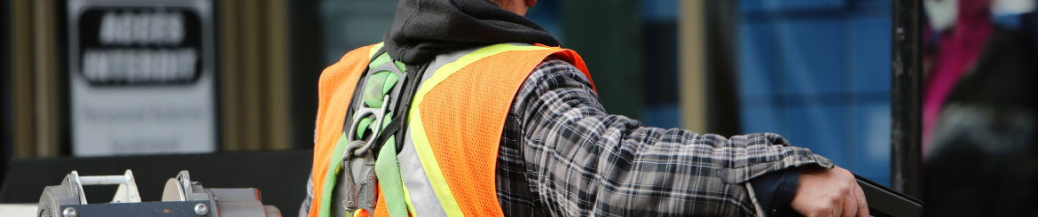 The back of a person wearing high vis and a harness looking towards a construction site