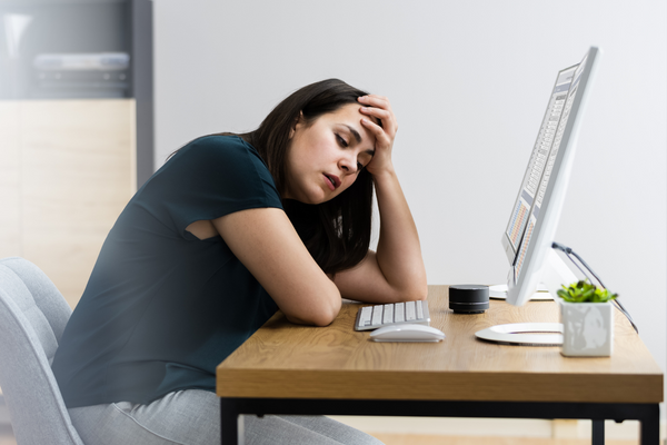 A stressed employee sat at their desk in front of their computer with their head in their hands