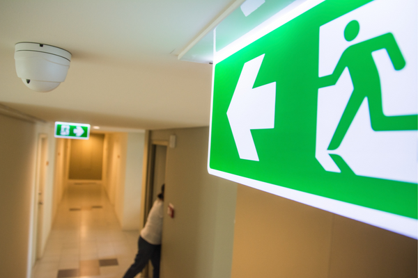 A close up of an illuminated green emergency exit sign pointing down a business corridor