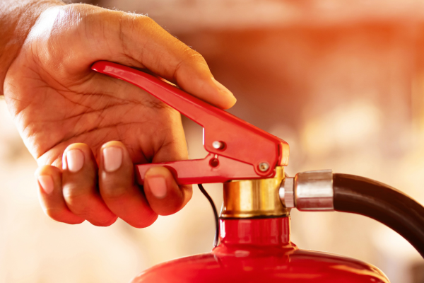 A close up of a hand holding the handle of a red fire extinguisher