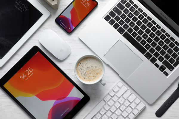 A flatlay of different devices on a table including an iPad, laptop and iPhone, with an all-important coffee in the middle